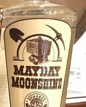 Mayday Moonshine bottle label with a mine cart, shovel and pickaxe
