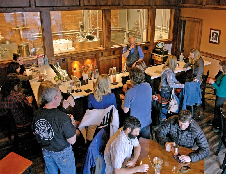 Guests at the Durango Craft Spirits tasting-room bar, with windows looking into the still room