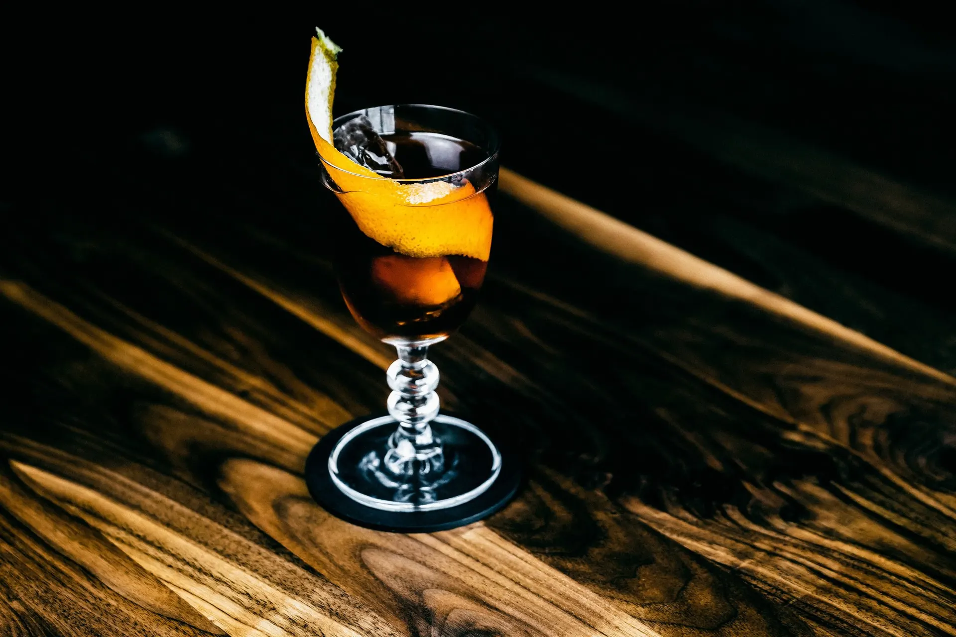 A craft cocktail with an orange twist on a dark wooden bar