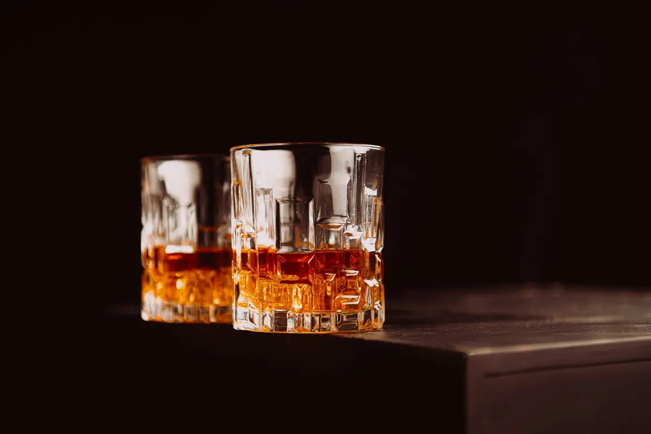 Two glasses of amber whiskey on a dark surface