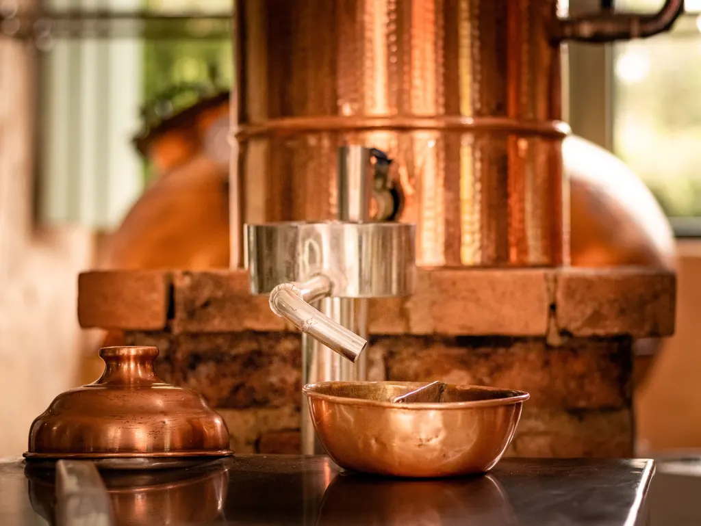 Hammered copper still above a steel spout and a copper collection bowl, set on a brick base