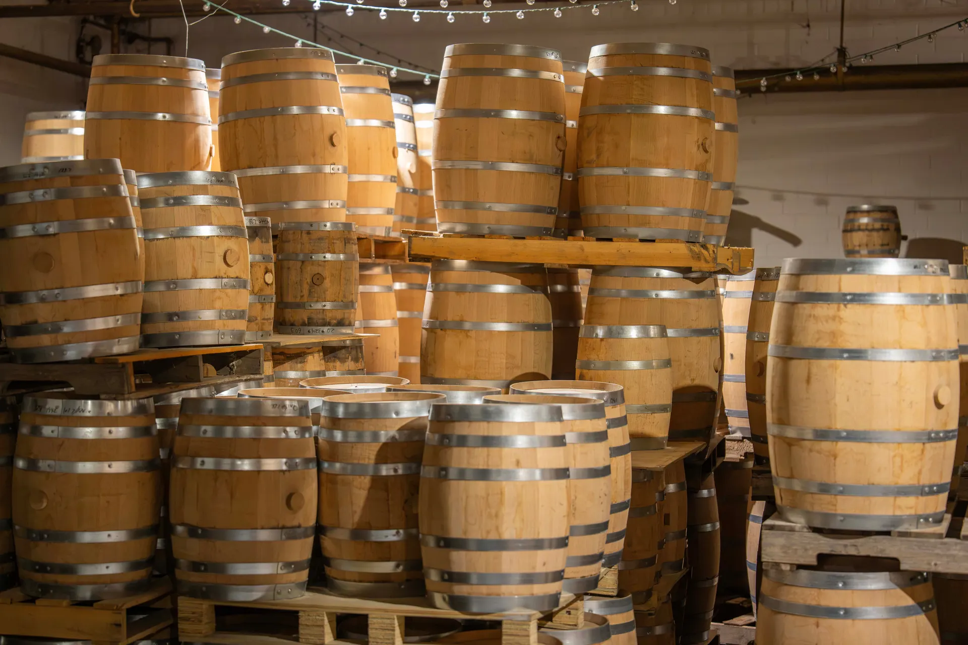 Stacked oak whiskey barrels with steel hoops in a warmly lit barrel room