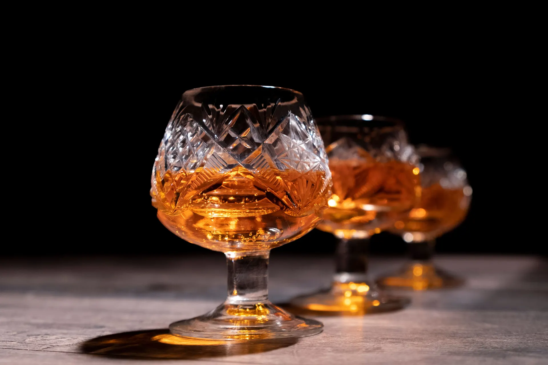 Cut-crystal snifters of amber whiskey on a stone bar against a dark backdrop